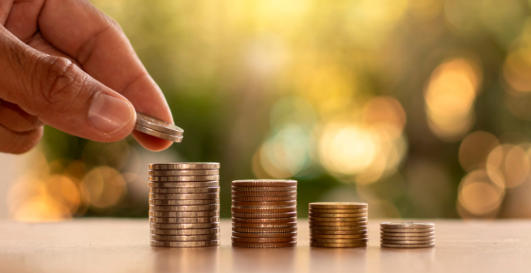A hand reacing out to place a coin on a stack of coins. There are smaller stacks of coins to the right.
