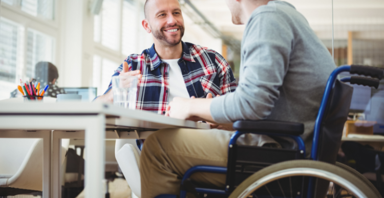 A person is sat at a table, talking to someone in a wheelchair