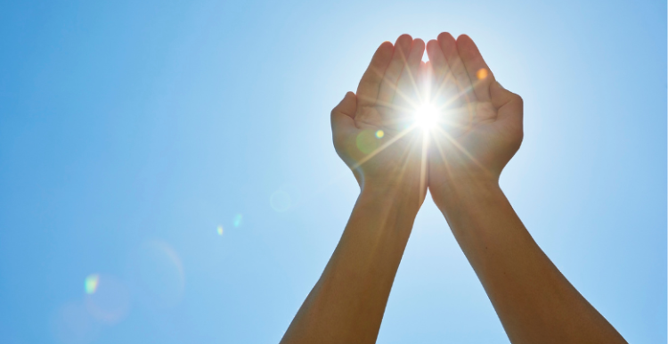 Two hands are raised towards the sun with the sunlight shining between the 2 open palms.