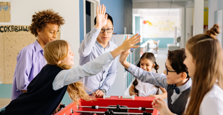 Teenagers at a table football game, high fiving each other.