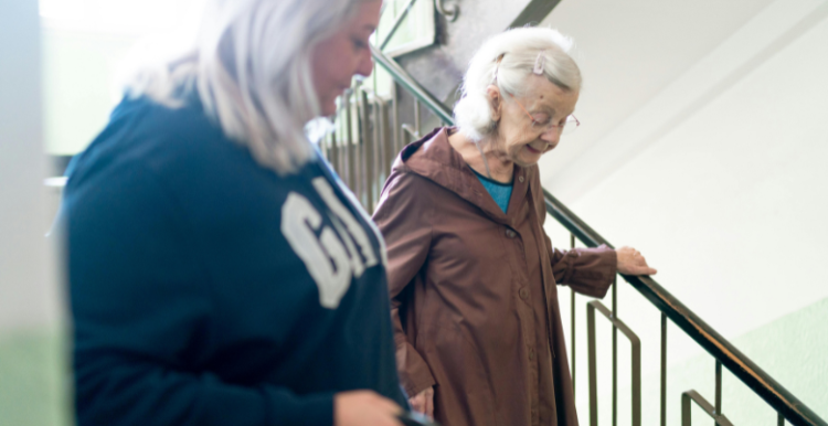 2 people going down some steps. The younger person is looking towards the older person, checking they are ok.