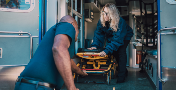 2 ambulance workers putting a stretcher back into an ambulance.