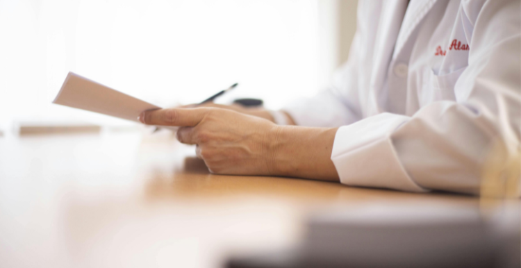 Shows someone in a white medical coat looking at a piece of paper they are holding in their hands