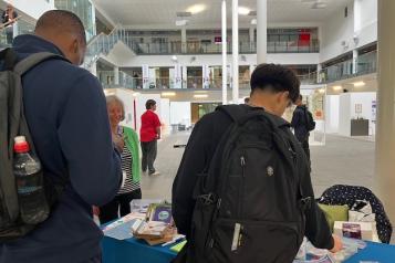 Two students looking at information on our table at a college. One of our volunteers, is talking to them.