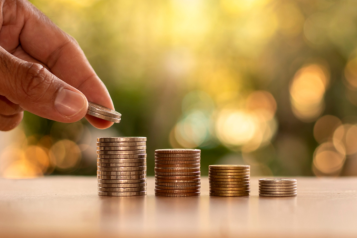 A hand reacing out to place a coin on a stack of coins. There are smaller stacks of coins to the right.