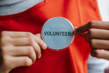 A person holding out a volunteer badge that is pinned to their Tshirt