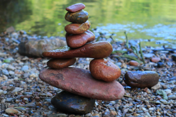 Photo of some rocks balancing on top and beside other rocks and flat stones. The rocks are beside some water.