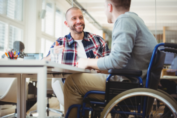 A person is sat at a table, talking to someone in a wheelchair