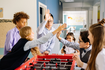 Teenagers at a table football game, high fiving each other.