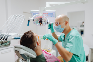 A dentist tending to a patient in a reclined dentist chair.