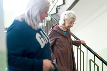 2 people going down some steps. The younger person is looking towards the older person, checking they are ok.