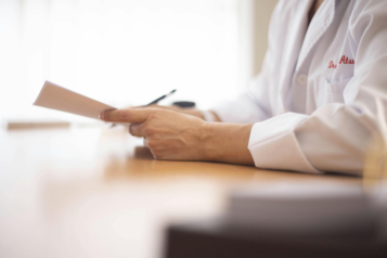 Shows someone in a white medical coat looking at a piece of paper they are holding in their hands