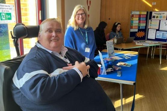 One of our volunteers is sat in his wheelchair facing the camera. Behind him is one of our Insight and Engagement Officers.