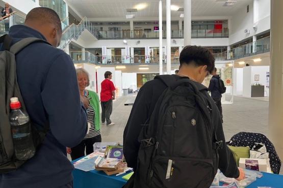 Two students looking at information on our table at a college. One of our volunteers, is talking to them.