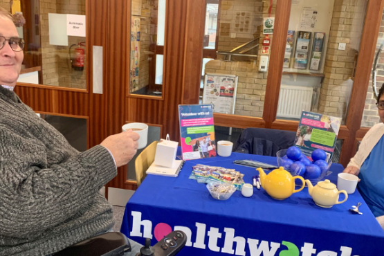 Two of our volunteers sitting at a Healthwatch Surrey branded table.