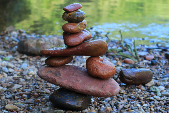 Photo of some rocks balancing on top and beside other rocks and flat stones. The rocks are beside some water.