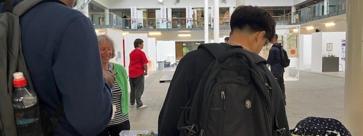 Two students looking at information on our table at a college. One of our volunteers, is talking to them.