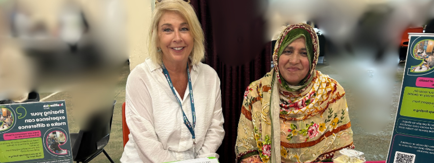 Our Insight and Engagement officer sat with a member of the community at a local mosque. In front of them is a table filled with Healthwatch Surrey information and merchandise
