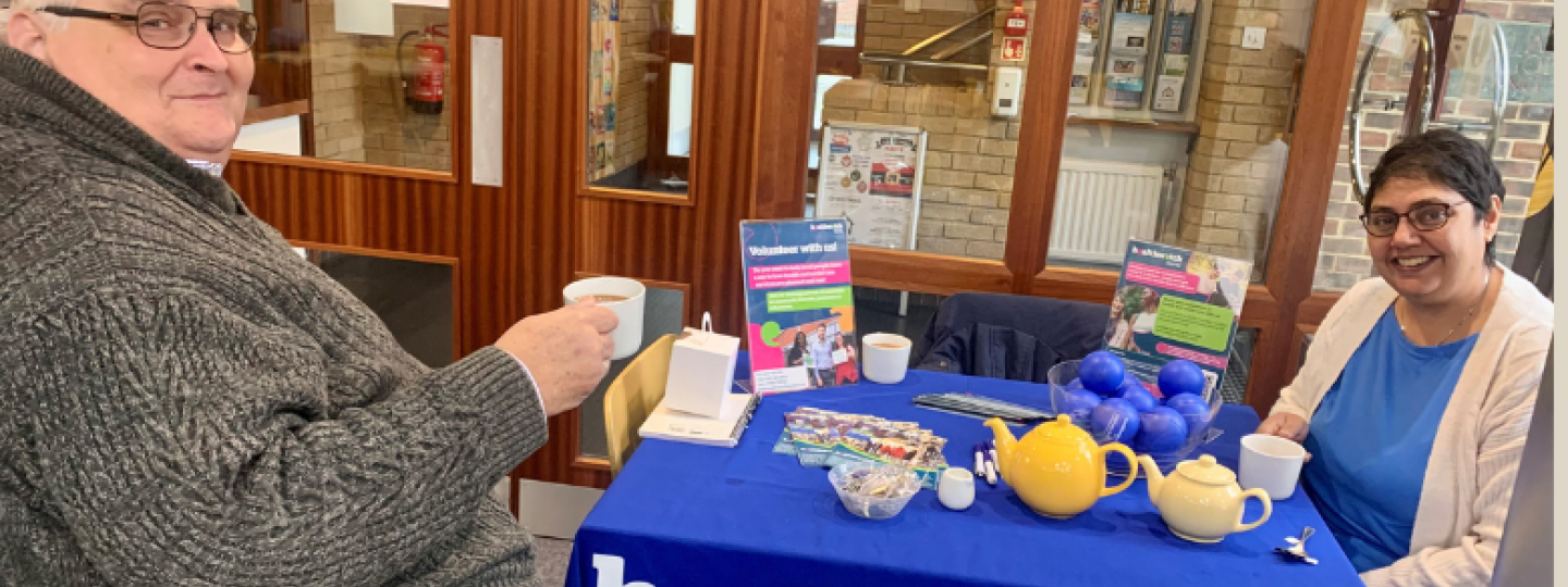Two of our volunteers sitting at a Healthwatch Surrey branded table.