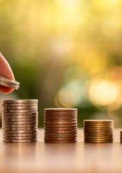 A hand reacing out to place a coin on a stack of coins. There are smaller stacks of coins to the right.
