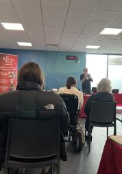 Photo of one of our engagements at a Slimming world meeting. The speaker can be seen at the front and then we can see the backs of everyone else as they are sitting facing him in the room.