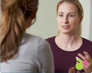 Image of a young woman speaking to another (facing away from the camera)