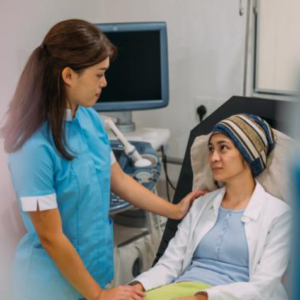 Person sitting in a hospital bed. A nurse is standing beside the bed holding her hand and touching her shoulder.