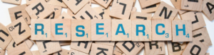The word Research is spelled out in Scrabble tiles. This word is set on a pile of other Scrabble tiles.