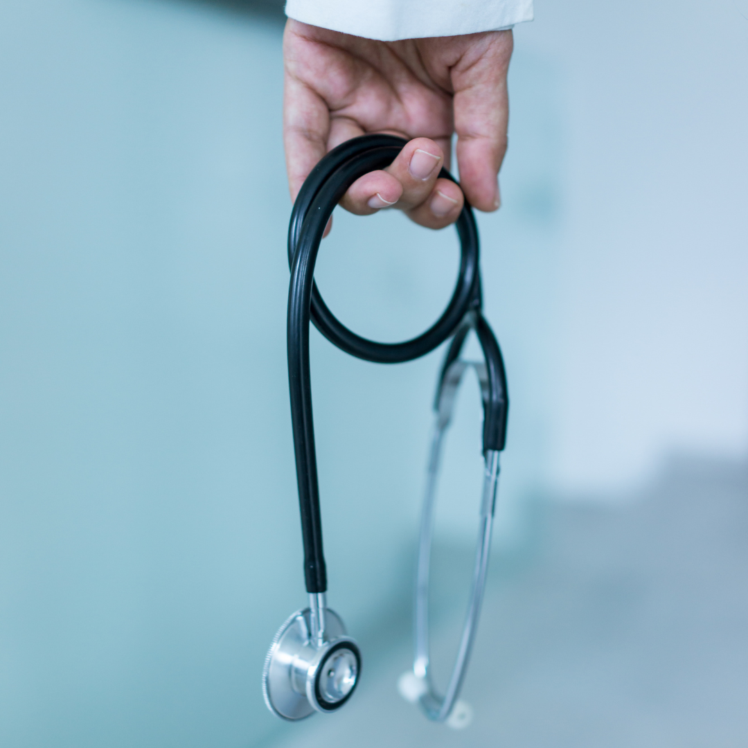 Photo of a hand holding stethoscope so that it is hanging down. You can just see the cuff of a white coat above the hand.