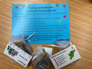 A photo of our certificate of thanks sent out to each of our volunteers and of the sweets we also sent to them. The certificate is on a pale blue background and starts with the words 'Thank you from all of the Healthwatch Surrey staff and then lists the ways our volunteers have supported us (detailed in the main text). At the top left and right are some banners and to the right of the certificate are 2 colourful stars. At the bottom are the logos of Volunteers week and Healthwatch Surrey. The sweets are wrapped in an organza bag, with labels attached saying thank you on one side, and then on the other with the words (each ending in ‘mint’ like to sweet) Achievemint, Commitmint, Encouragemint, Investmint, Involvemint)