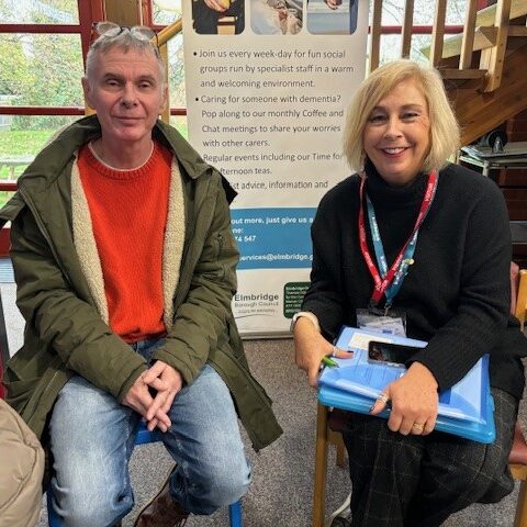 One of our Insight and Engagement Officers and a member of the public are sat next to each other and smiling at the camera. Our Insight and Engagement Officer has a clipboard in her hand.